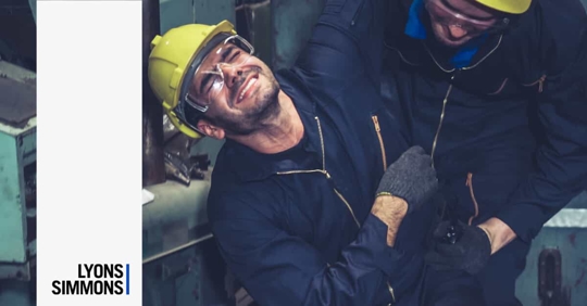One Man Holding Another in Pain at an Industrial Plant